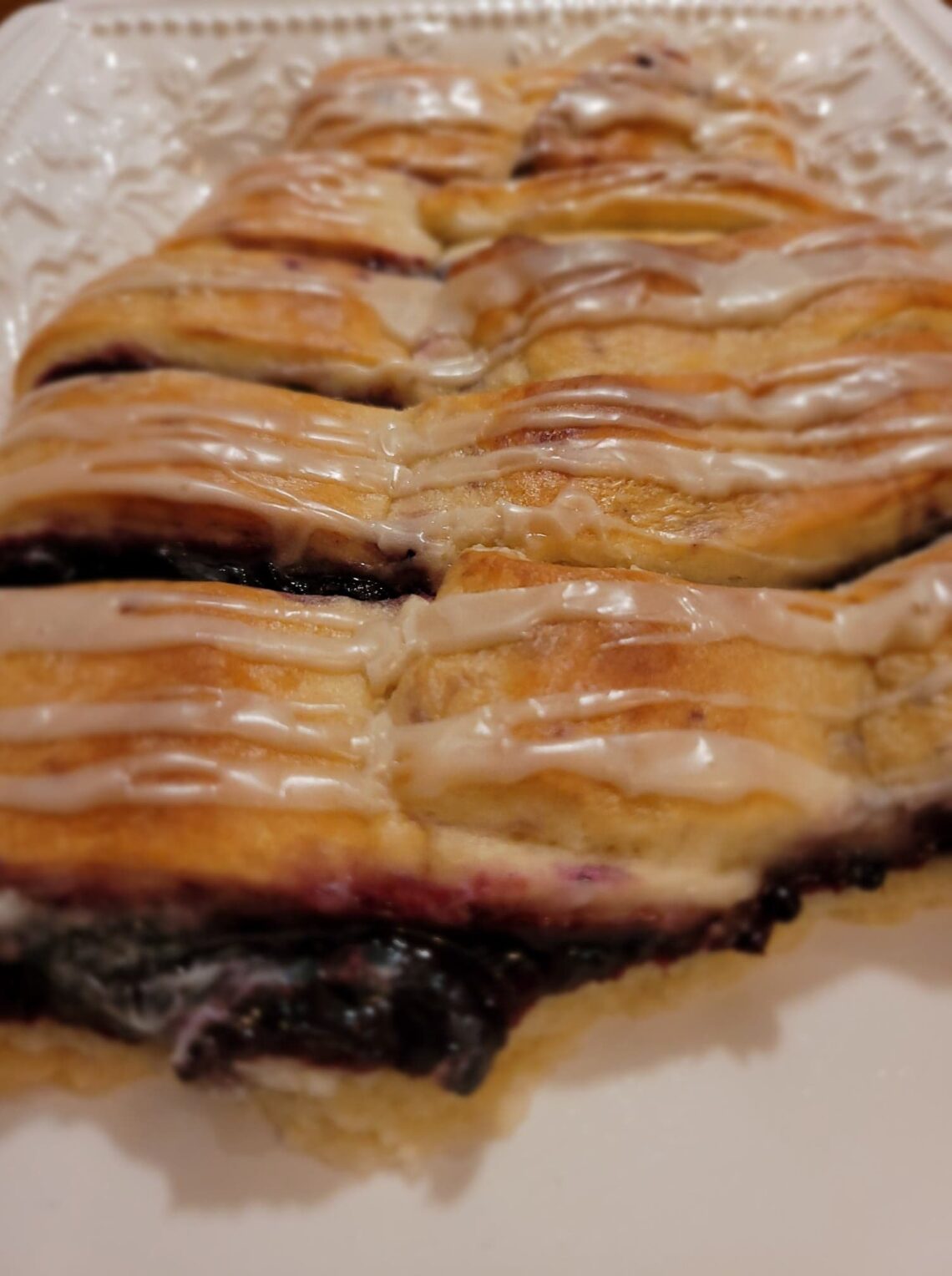 Photo of blackberry danish on a long rectangle shaped plate. The danish has a white icing drizzled on top.